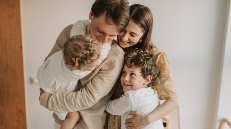 Photo of man, woman and two children hugging and smiling each other