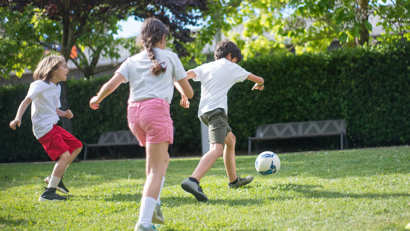 Three children playing football outside.