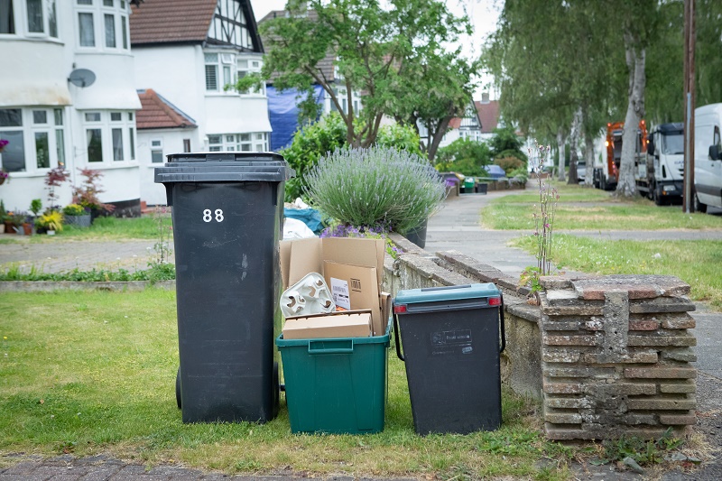 Waste bins in a front garden by a brick wall.