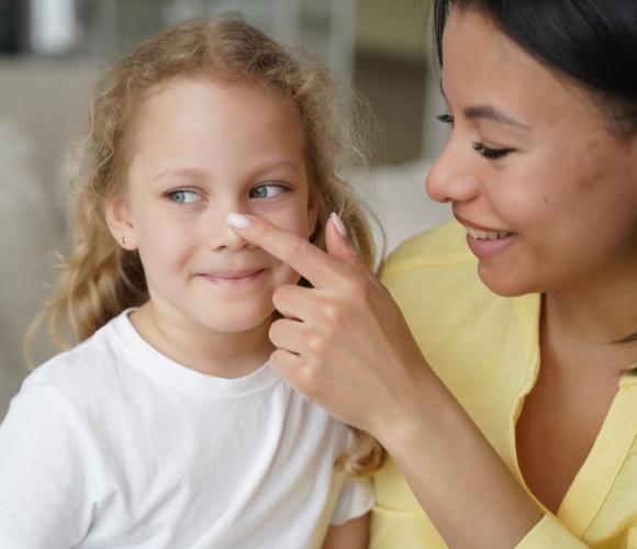 A foster carer in a yellow dress gently touching the cheek of a young person wearing a white shirt, sitting together indoors.