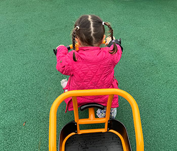 Child in bright pink jacket riding orange tricycle.