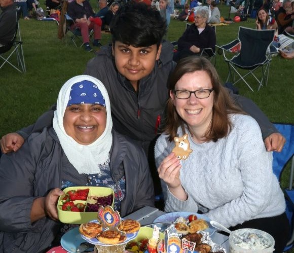 Image shows two adults and a young person enjoying a picnic.