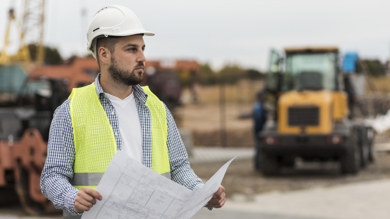 Man on site wearing safety jacket and hat.