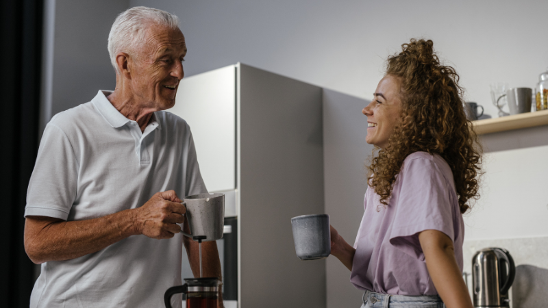Photo of a man and a woman stood together in a kitchen while holding cups of tea/coffee.