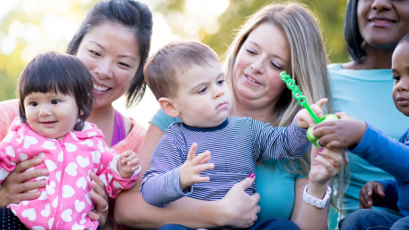 Photo of three mothers and their three children sat together playing with bubble wands.