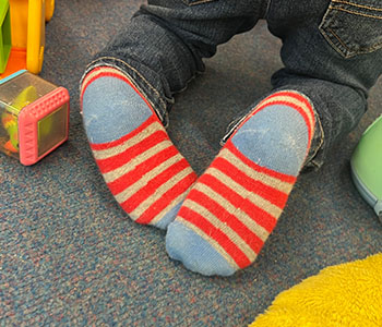 Child kneeling on the ground’s feet in in red, grey and blue striped socks.