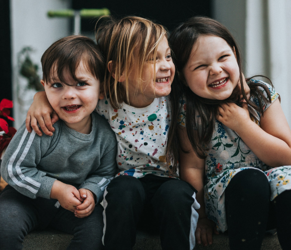 Image shows 3 children with their arms around each other smiling.