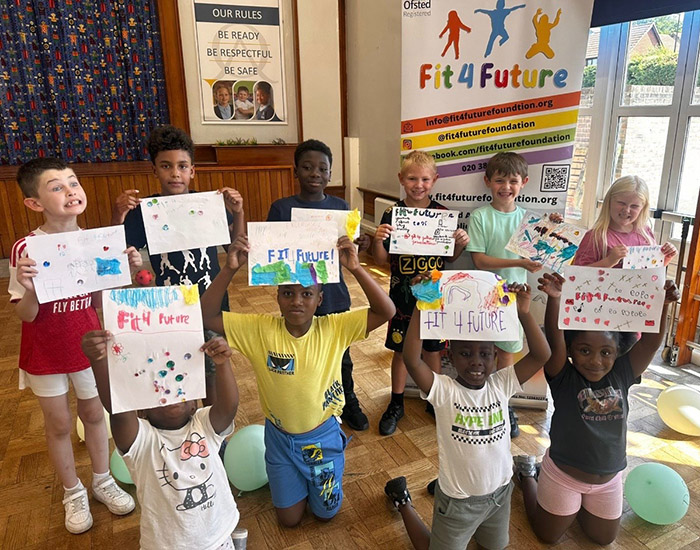 Fit 4 Future - Mottingham Community Centre: Photo of a group of children in a community hall holding up hand drawn Fit 4 Future posters.