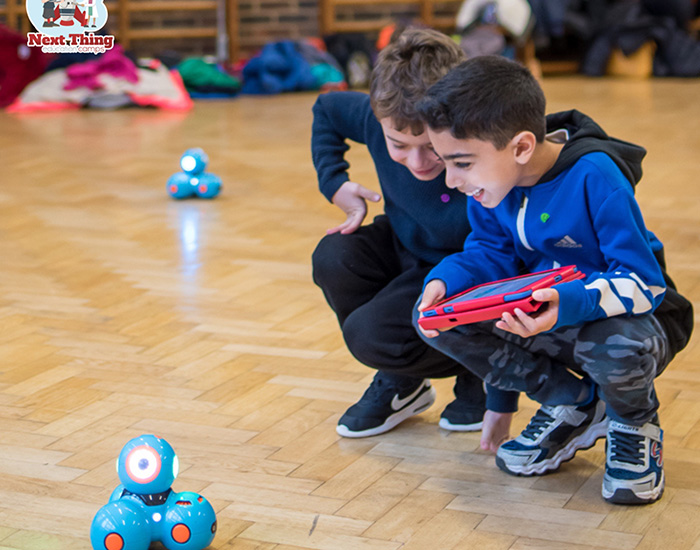 Next Thing Education - WOW Tech - Trinity Primary: Photo of two children playing with a robot toy while holding a tablet to control the robot.