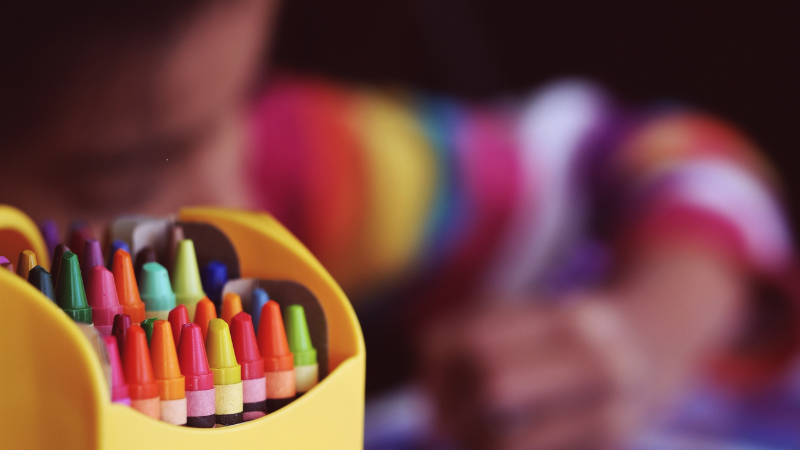Crayons in focus. The background image is blurred with child drawing.