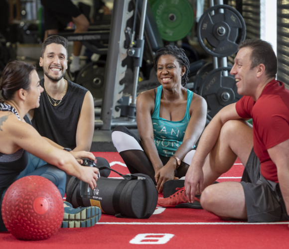 People sitting in a gym with gym equipment.