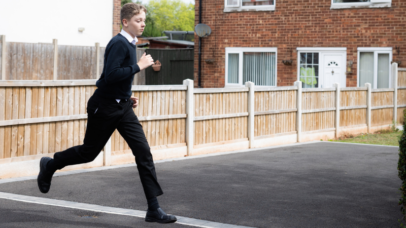 Photo of young boy running through a neighbourhood in their school uniform.