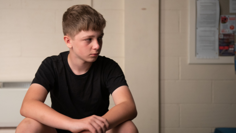 Photo of young boy sat in a room looking off to the side.