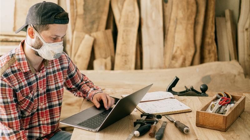 Carpenter wearing a mask, sitting at a laptop.