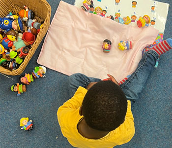 A child sitting on the carpet completing a task with little people figurines.