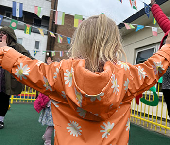 Child in orange coat with daisies on, with their arms out to the side.