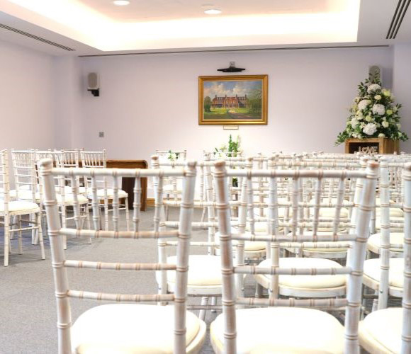 An angled view of the ceremony room including chairs, flowers and picture.