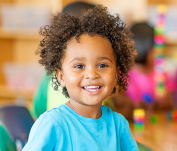 A young girl in a bright blue t-shirt with a big smile on her face holding a colourful toy.