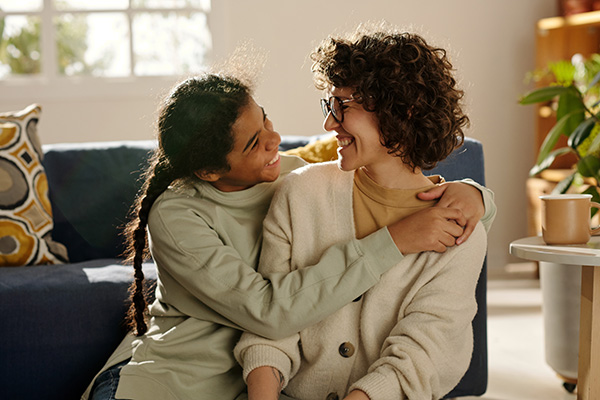 Young person hugging their foster carer while sitting together at home.