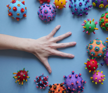 Photo of a hand laid flat on a table with illustrated representations of germs and diseases in various shapes and colours surrounding the hand.