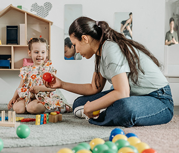 Adult playing with a young child indoors using toys.