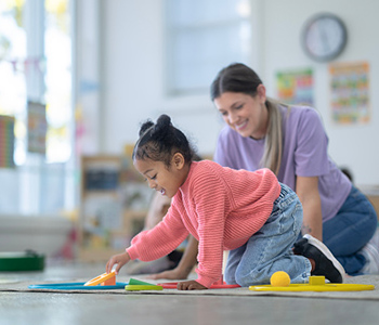 Child playing with toys in an early years setting, with an adult supporting them.