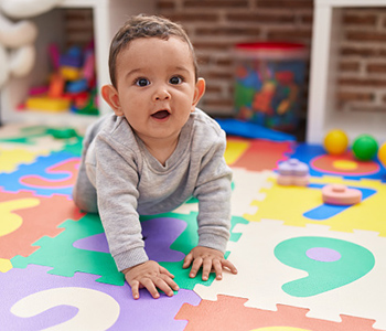 Baby crawling on a colourful play mat in an early years setting.