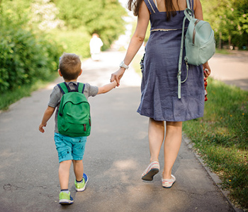 Adult and young child walking hand in hand along a path outdoors.