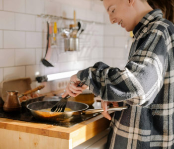 Young person cooking in a kitchen, stirring food in a frying pan.