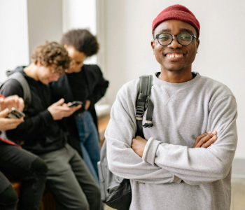 A smiling young man in a red beanie and glasses with friends in the background, highlighting friendship.