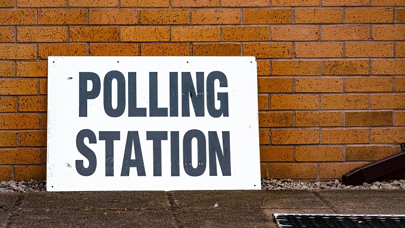 Polling station sign leaning up against a brick wall.