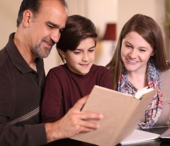 Middle age foster carer couple with a young teenager, helping him with homework.