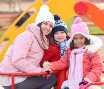 Young foster carer playing with her birth child and foster child in the park.