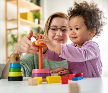Single foster care mother playing stacking a tower with a young baby in her care.