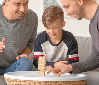 Same gender foster couple playing Jenga with a young foster boy.