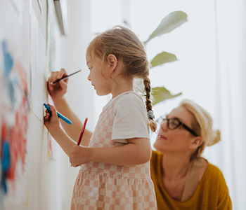 Child drawing on a board with an adult supporting them.