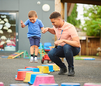 Child taking part in an outdoor activity with a childcare worker at a pre-school.