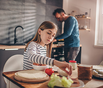 A young girl who is representing a young carer for a male adult. The girl is preparing his food.